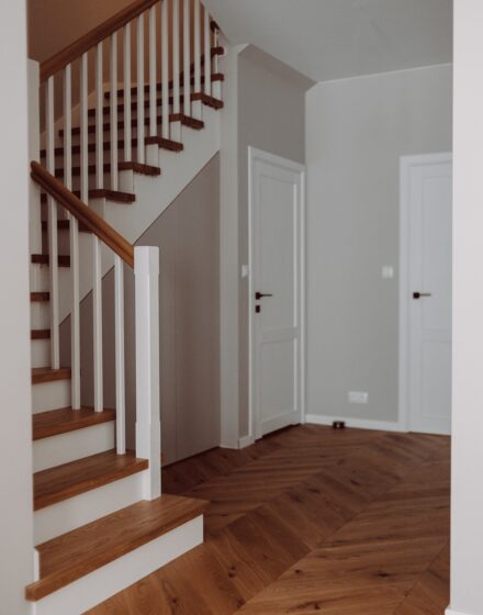 Chevron parketo grindys, mediniai laiptai ir skandinaviško stiliaus durys - derinys, suteikiantis kambariui modernumo.